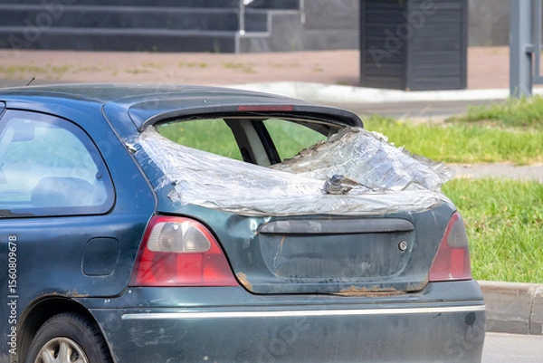 Fototapeta Old car with broken rear window covered with plastic film, parked on the side of a city road, realistic photo style, daylight outside, vehicle damage concept