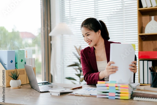 Fototapeta Female employee working with pile of documents to search for information and check documents on desk in office. Accounting income, expenses, tax records and hard work.