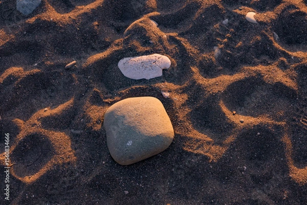 Fototapeta A close-up view of smooth stones resting on a sandy beach. Illuminated by warm sunlight. Making it ideal for themes related to nature, relaxation and coastal landscapes.