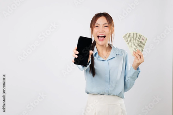 Fototapeta Smiling happy woman showing phone screen and holding money, mobile online app money gain representing financial success and digital achievement with confidence. isolated studio white background