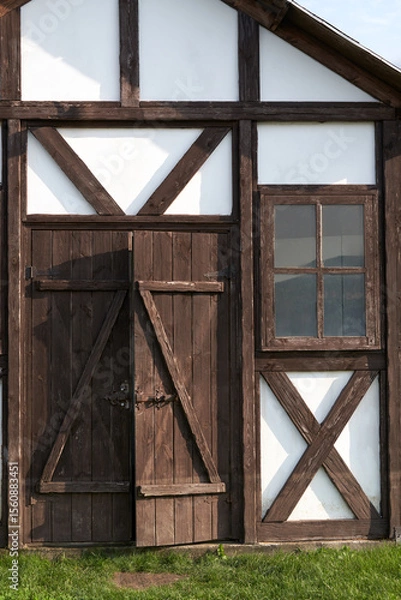 Fototapeta A fragment of the facade of a vintage wooden building: a plank entrance door with a bolt lock and a window in a brown wooden frame.