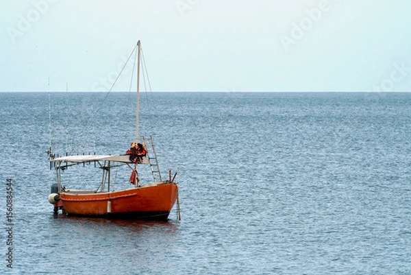 Fototapeta Sea fishing. A lonely red boat with many different fishing rods on board is anchored in the middle of the sea.