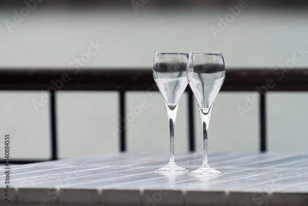 Fototapeta Two transparent Trumpet-shaped glasses on a table in a summer cafe by the lake.