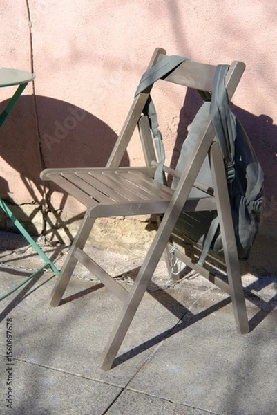 Fototapeta Wooden chair with hanging green backpack near cafe table, outdoor coffe break in spring or summer city. First warm days and open terraces on streets. Rest pause during walk