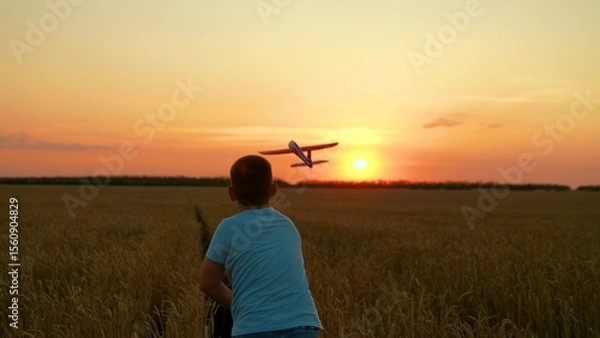 Obraz Dreaming boy throws toy airplane into flight child plays in wheat field sunset. Child dreams of fly travel. Child plays with toy airplane. Child boy wants to travel around world, sun sky. Slow motion