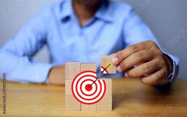 Fototapeta Businessman set goal by arranging wooden dice into dartboard icon conveying the challenge of higher sales targets and making more profit
