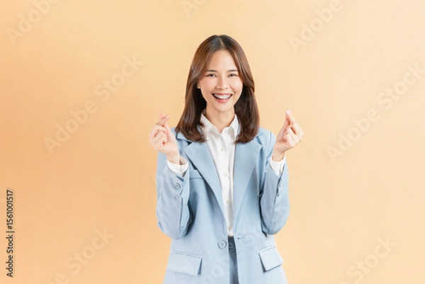 Fototapeta Cheerful beautiful Asian business woman showing mini heart sign on beige color background, love concept.