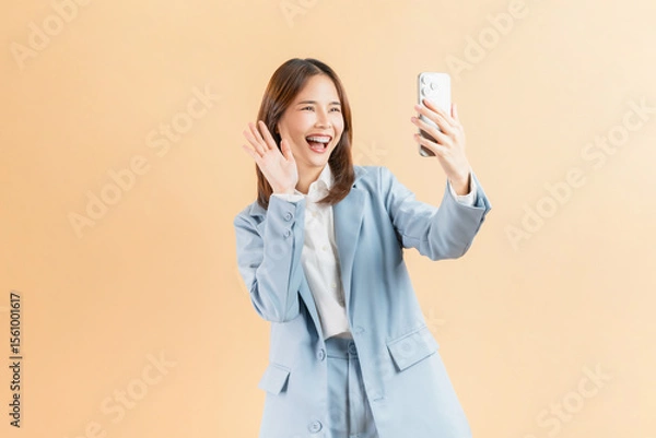 Fototapeta Confident Asian businesswoman using smartphone at video call friends online through the internet on beige color background.
