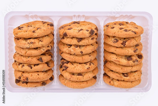 Obraz Stacked chocolate chip cookies in a clear plastic tray on a white background. Crunchy golden biscuits perfect for snack, packaging design, bakery display or dessert advertising visuals.