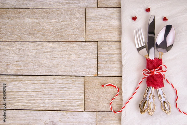 Obraz Elegant vintage cutlery tied with red ribbon and tiny hearts on a white napkin over rustic wood. Perfect romantic table setting for Valentine’s Day, wedding dinner or festive love celebration.