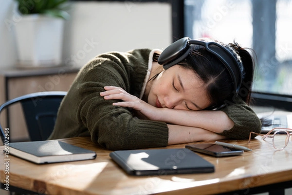 Obraz Tired female student with headphone sleeping at desk after hard learning