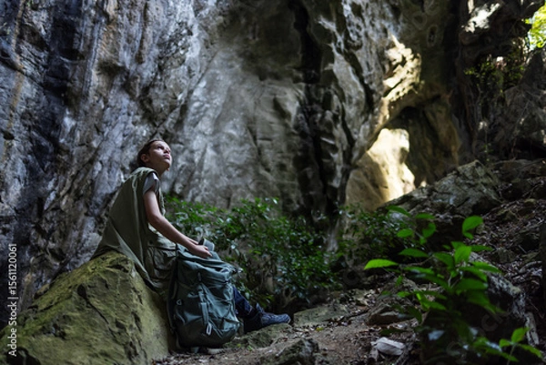 Obraz A hiker rests on a mossy rock inside a rocky canyon, surrounded by lush greenery. The peaceful scene captures a moment of solitude, reflection, and connection with nature during an outdoor adventure.