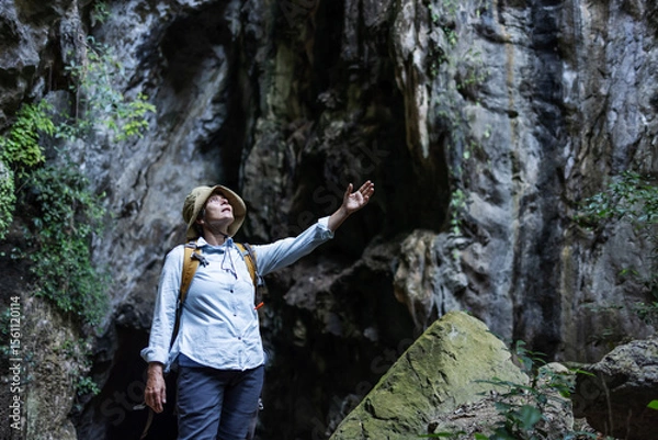 Obraz A joyful hiker stands with arms raised inside a rocky canyon, surrounded by lush vegetation. The scene captures freedom, triumph, and a deep connection with nature during an adventurous journey.