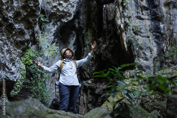 Obraz A joyful hiker stands with arms raised inside a rocky canyon, surrounded by lush vegetation. The scene captures freedom, triumph, and a deep connection with nature during an adventurous journey.