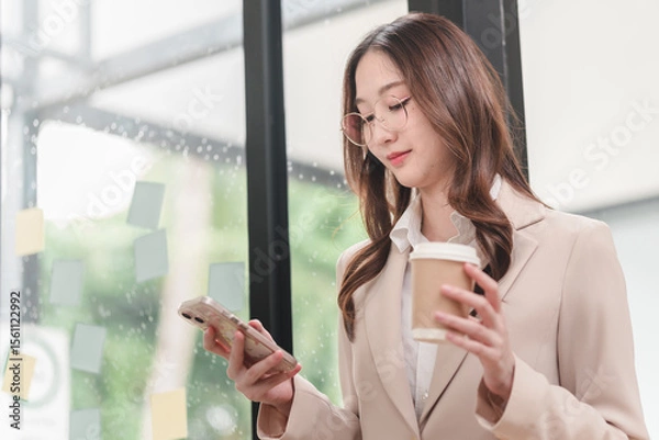 Obraz Professional woman engages with smartphone while enjoying coffee in modern workspace setting