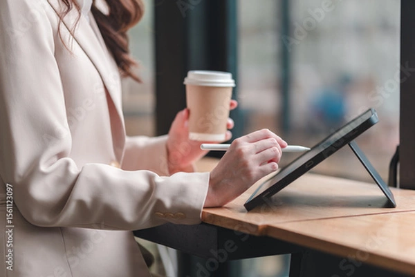 Obraz Professional woman engages with digital tablet while enjoying coffee at modern workspace