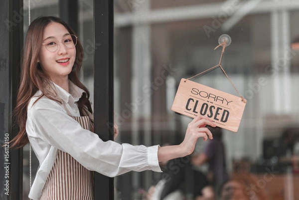 Obraz Smiling employee holds closed sign to inform customers of business hours