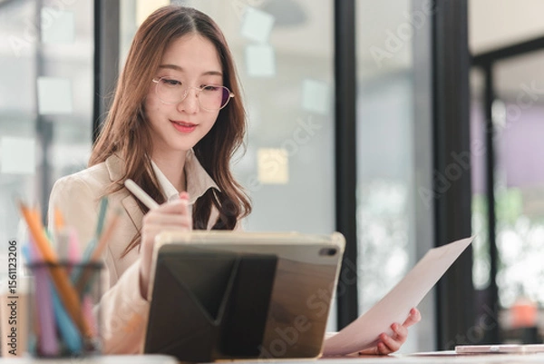 Obraz Young professional engages in creative work with tablet and notepad in modern office environment