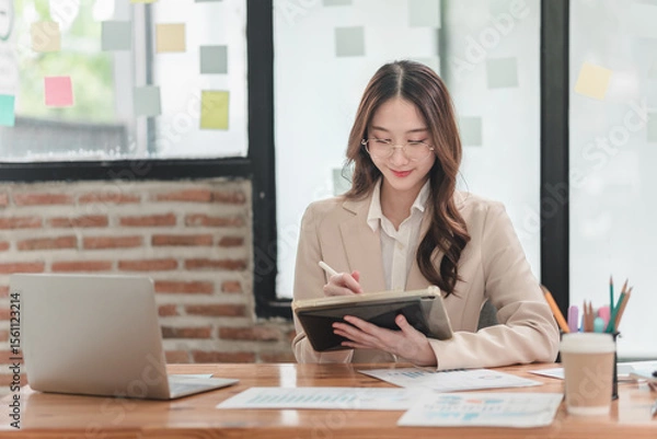 Obraz Professional woman engages in creative planning at modern office desk with laptops and colorful notes