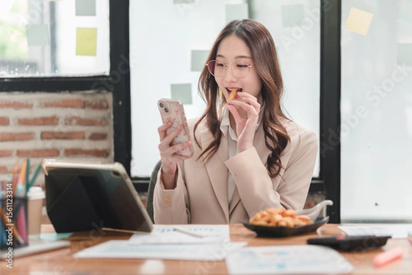 Obraz Professional woman engages with smartphone while enjoying snacks in a modern workspace environment