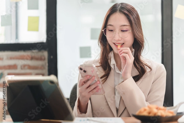 Obraz Young professional enjoys snack while engaging with smartphone in modern workspace setting
