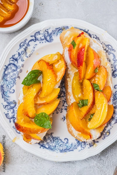 Fototapeta Bruschetta with ricotta cheese, sliced nectarines, basil and honey on a plate
