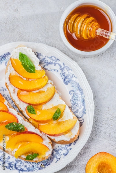 Fototapeta Bruschetta with ricotta cheese, sliced nectarines, basil and honey on a plate