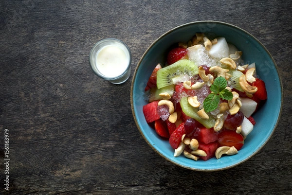 Fototapeta A bowl of colorful fruit salad with a combination of watermelon, strawberries, kiwi, grapes and garnished with mint leaves and cashew nuts