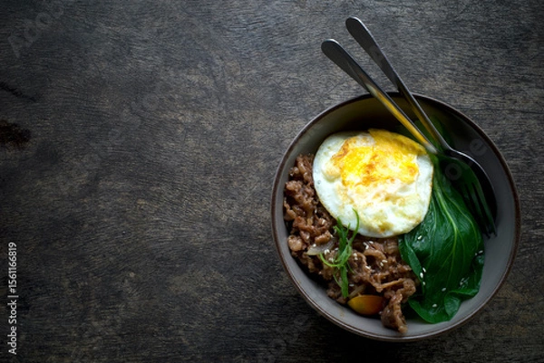 Fototapeta A bowl of food with a fried egg, savory beef and a green vegetable