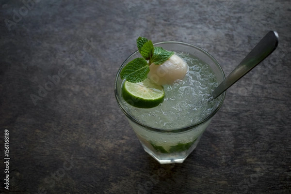 Fototapeta A glass of lemon water with ice garnished with lychee, sliced lemon and mint leaves