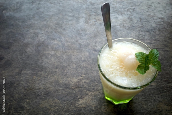 Fototapeta A glass of refreshing lychee drink with lime, mint leaves and ice, on wooden table