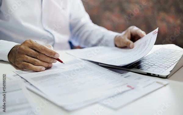 Fototapeta asian businessman holding pen reviewing document and business contract on desk in office using computer laptop working and meeting online