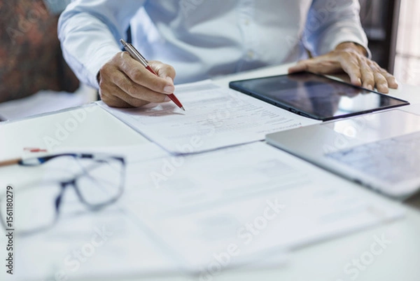 Fototapeta asian businessman checking document and business contract using tablet and laptop working on desk in office