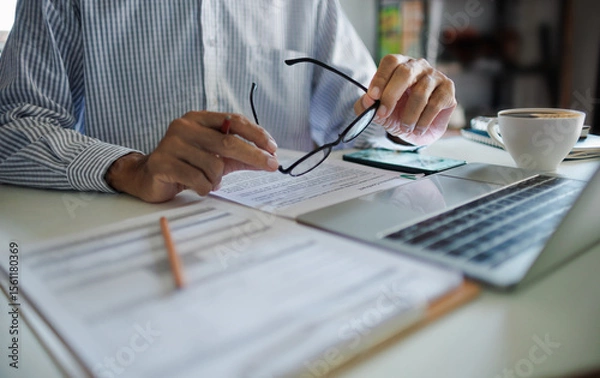 Fototapeta asian businessman holding eyeglasses working and meeting online with business group via laptop on desk at home office, working at home concept