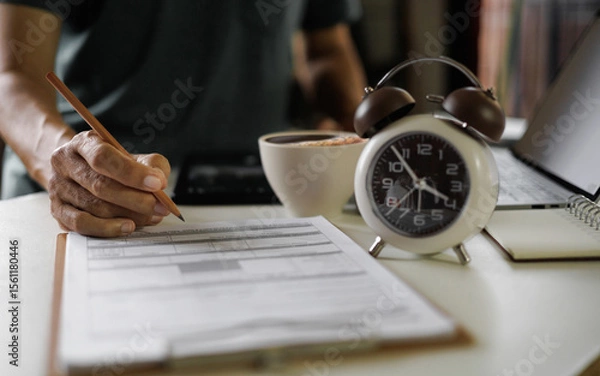 Fototapeta asian man work at home checking report document using laptop working in a hurry before end time in a day, time management concept, routine work, office hour