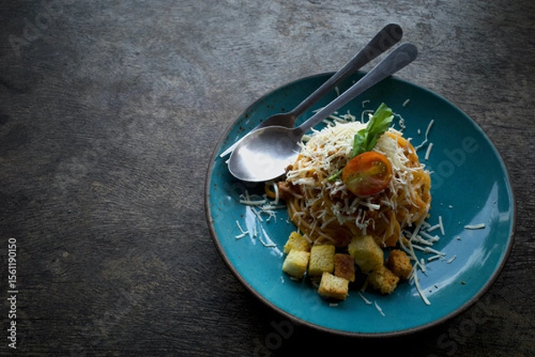 Fototapeta Volcano shaped Spaghetti in blue plate garnished with celery leaves, cheese, biscuits and sliced ​​tomatoes