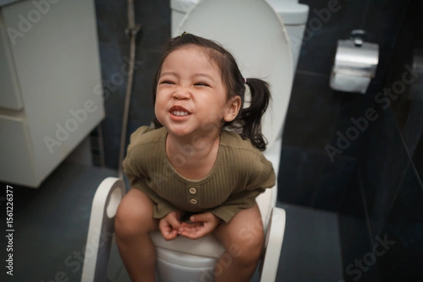 Fototapeta toddler girl sitting on toilet at home and suffering from stomachache and constipation