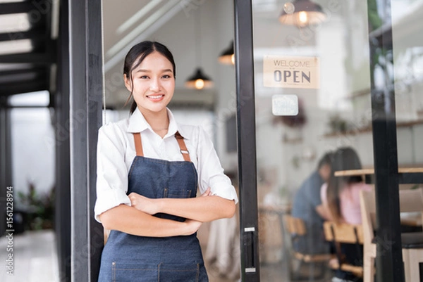 Obraz Portrait of smiling waitress standing with arms crossed at her shop