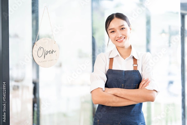 Fototapeta Portrait of smiling waitress standing with arms crossed at her shop