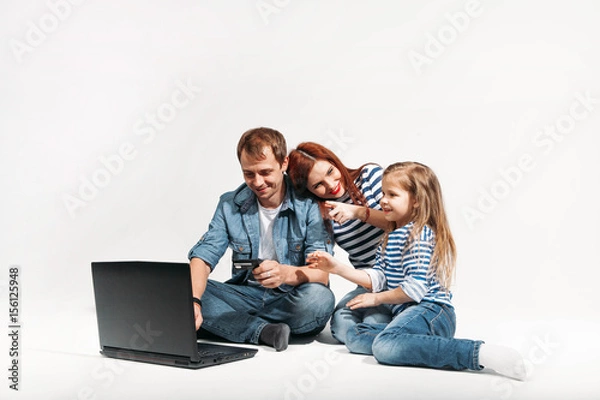 Fototapeta Happy family Father, mother and child lying on the floor with laptop and credit card on white background isolated
