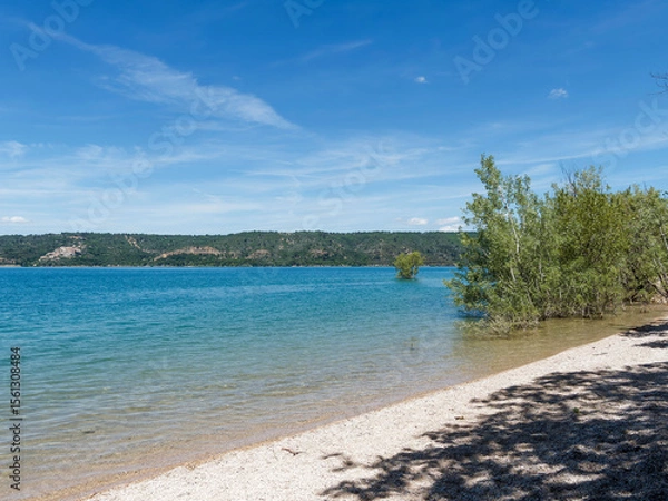 Fototapeta  Parc Régional du Verdon. Petite plage de sable au bord du lac de Sainte-Croix entre Bauduen et Costebelle avec vue le village Sainte-Croix-du Verdon à l'horizon. 

