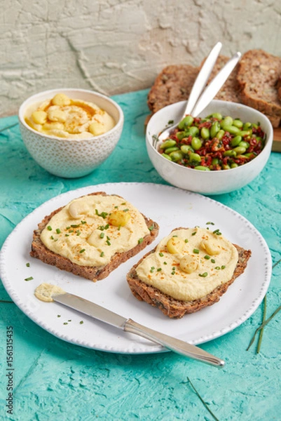 Fototapeta Hummus on bread slices with edamame salad in a bowl