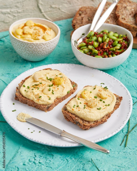 Fototapeta Hummus on bread slices with edamame salad in a bowl