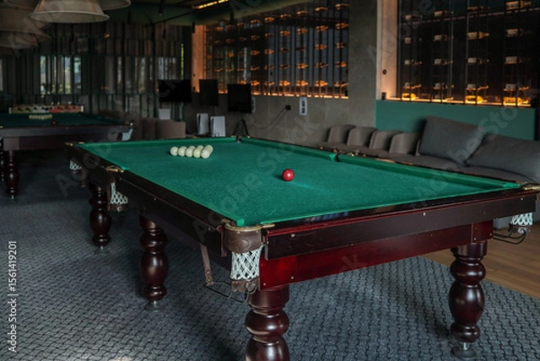 Fototapeta Cozy billiard room featuring classic green-felt pool tables; red and white balls arranged for play beneath soft pendant lamps in a modern hotel leisure space