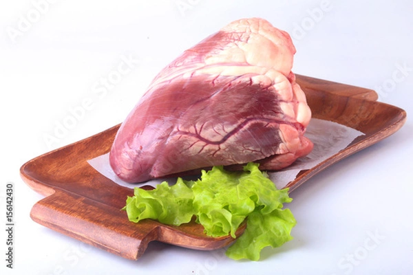 Obraz Raw beef heart and lettuce leaf on wooden desk isolated on white background from above and copy space. ready for cooking.