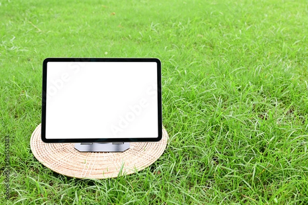 Obraz A tablet mockup with a large blank display, placed on a lush grassy meadow under a bright blue sky