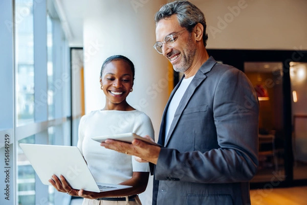 Fototapeta Smiling business professionals sharing ideas while working with laptops and tablets