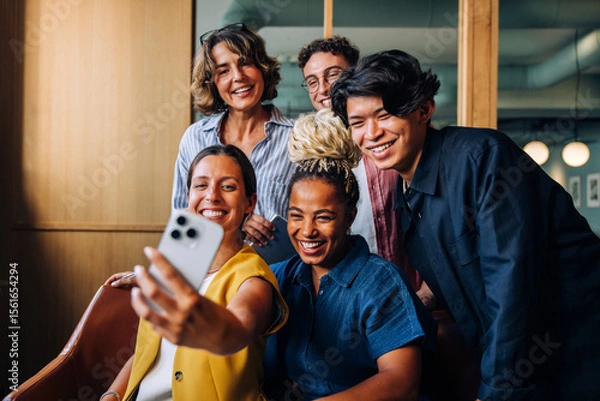 Fototapeta Group of diverse colleagues smiling and taking a selfie indoors