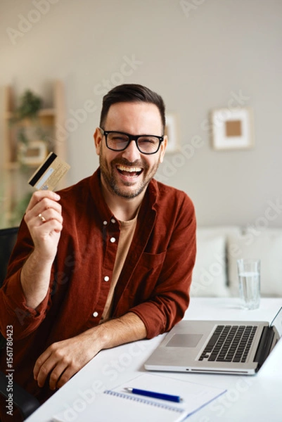 Obraz Happy entrepreneur showing credit card while working remotely from home
