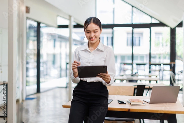 Obraz Young pensive Asian business woman professional manager executive leader holding digital tablet standing in corporate office,thinking of solution, lost in thoughts.
